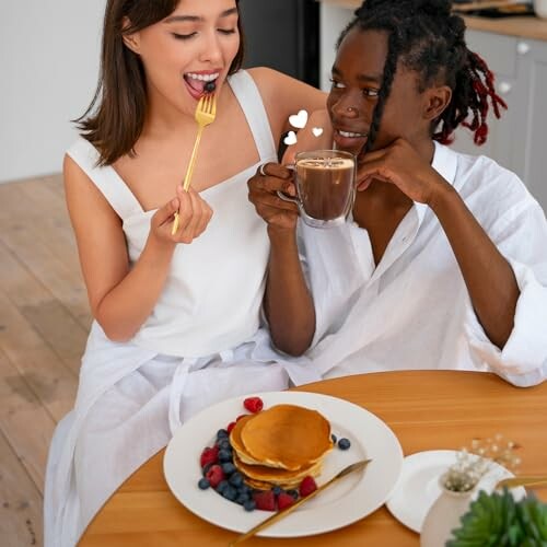 Couple enjoying pancakes and hot chocolate at breakfast table.