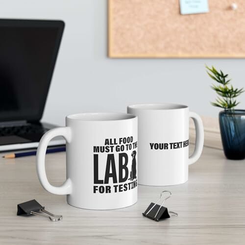 Two custom mugs on an office desk with a laptop and clipboards.