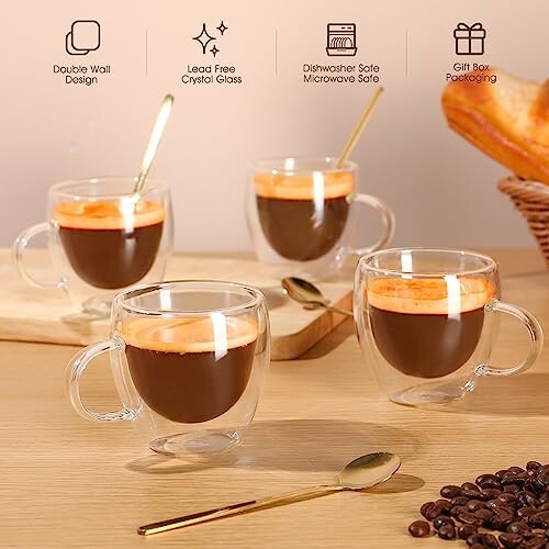 Four double-wall espresso glasses with coffee and gold spoons on a wooden table.