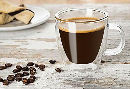 Double-walled glass cup of coffee with coffee beans and pastry.