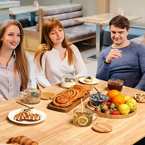 Three friends at a cafe table with pastries, fruit, and drinks.