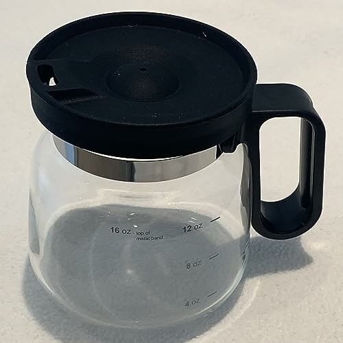 Glass coffee pot with black lid and handle on a light surface.