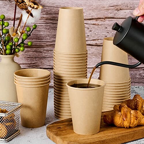 Stack of paper cups with coffee being poured, next to croissants.